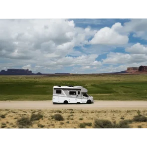 Thor Tiburon Sprinter Reisemobil fährt durch eine offene Grünlandschaft mit markanten Felsformationen im Hintergrund.