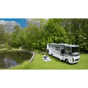 Thor Windsport 2026 Wohnmobil, geparkt auf einer grünen Wiese neben einem See, umgeben von Bäumen, mit ausgeklappten Campingmöbeln.
