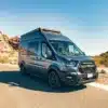 Trinity Ford Transit Trail Camper Van auf einer Straße mit Felsen im Hintergrund