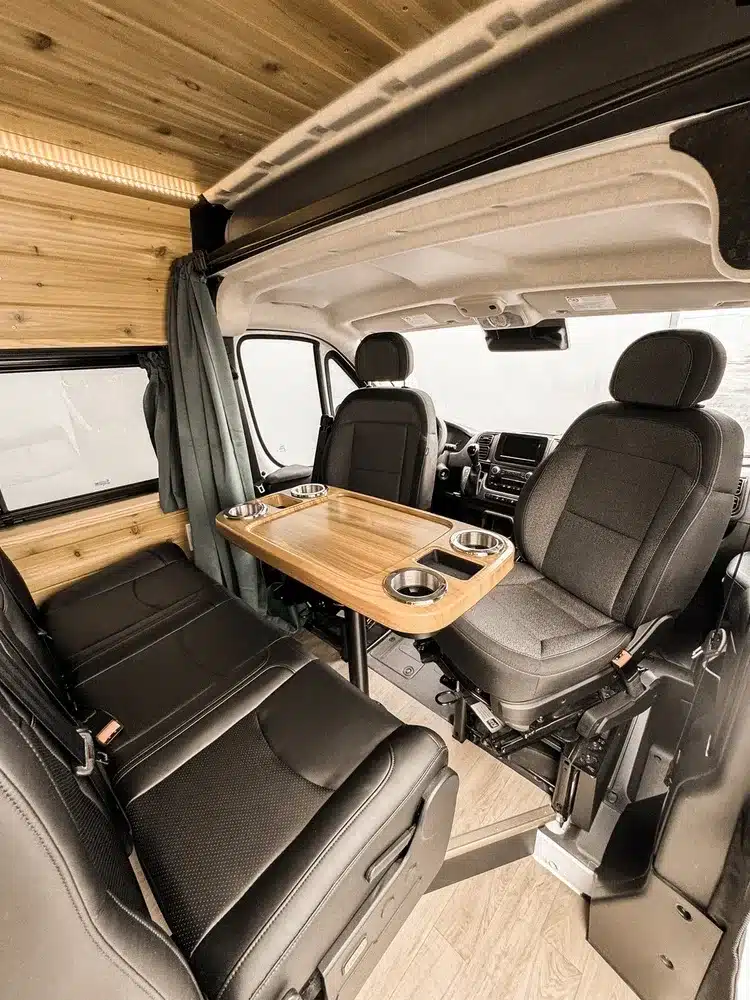 Gemütlicher Wohnbereich im RAM Promaster 2500 Camper mit Dreier-Sitzbank, Tisch und zwei drehbaren Vordersitzen.