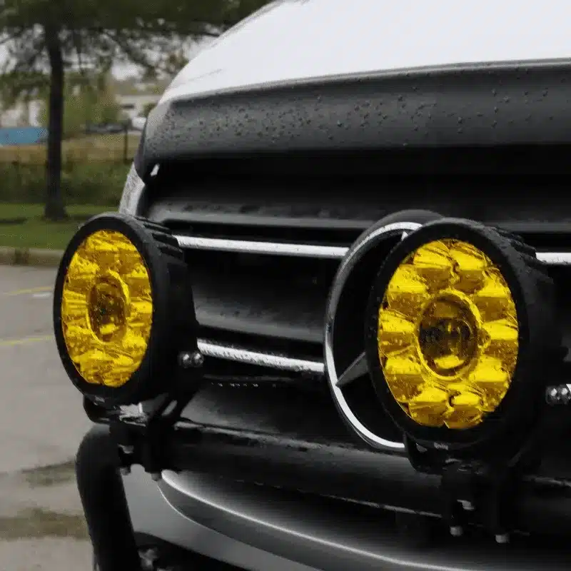 Nahaufnahme von zwei gelben Zusatzscheinwerfern an der Front eines Mercedes Sprinter unter nassen Bedingungen