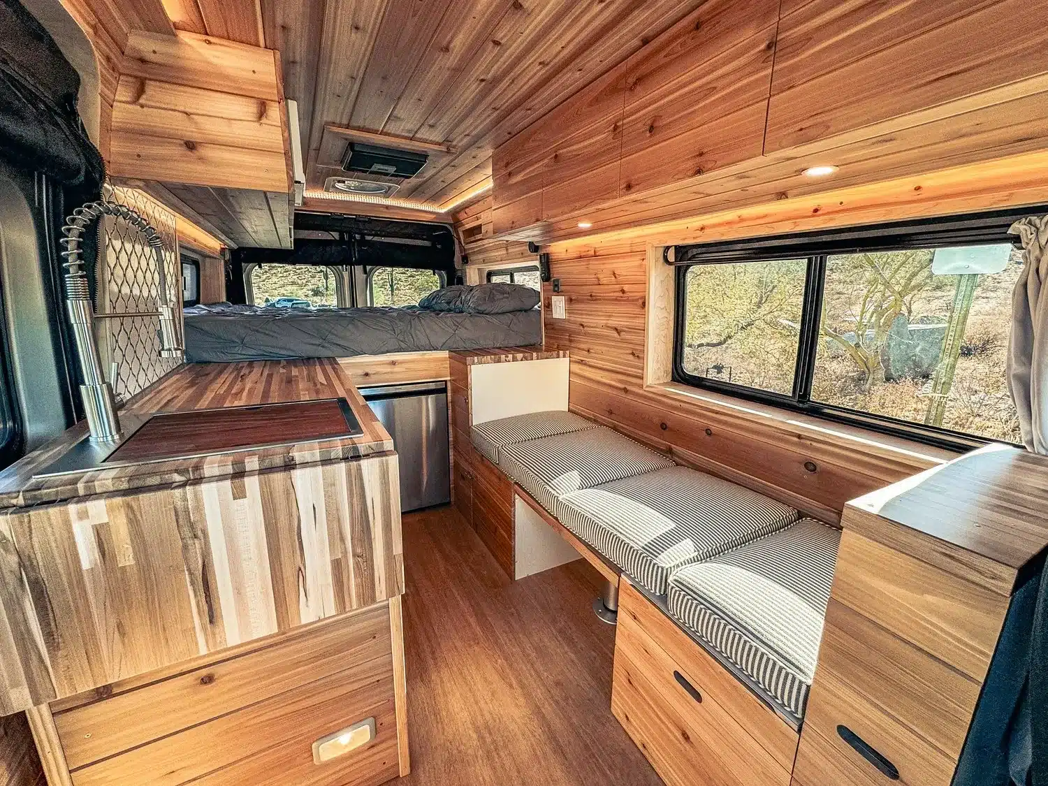 Innenraum eines Vandiamo-Kastenwagen-Campers mit Küche, Sitzbank und Schlafbereich, komplett in Holz ausgebaut.