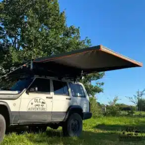 Eine freitragende Seitenmarkise ist an der Seite eines Offroad-Fahrzeugs montiert und spendet Schatten auf einer Wiese.