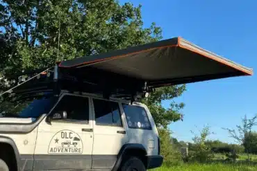 Eine freitragende Seitenmarkise ist an der Seite eines Offroad-Fahrzeugs montiert und spendet Schatten auf einer Wiese.
