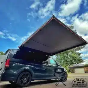 Montierte freitragende Seitenmarkise an einem schwarzen Van unter blauem Himmel, ideal für Camping und Outdoor.