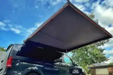 Montierte freitragende Seitenmarkise an einem schwarzen Van unter blauem Himmel, ideal für Camping und Outdoor.