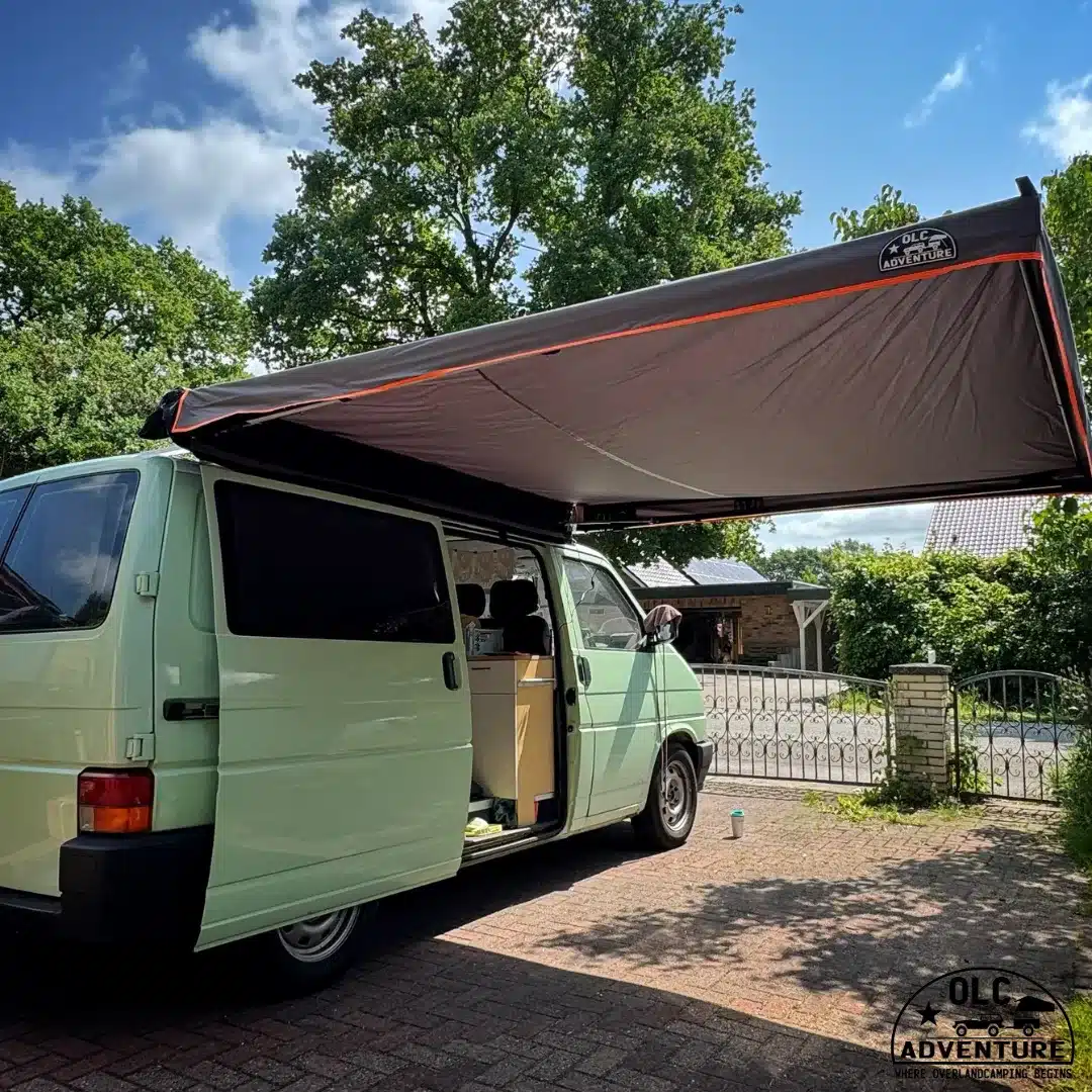Freitragende Seitenmarkise von OLC Adventure an einem hellgrünen Campingbus auf einem Stellplatz, seitlich ausgefahren.