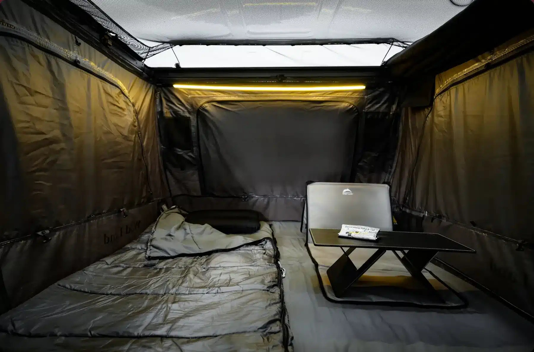 Innenraum eines Wild Land Sky Rover Dachzelts mit aufgeklapptem transparentem Dach, Schlafbereich, tragbarer Lounge und kleinem Tisch