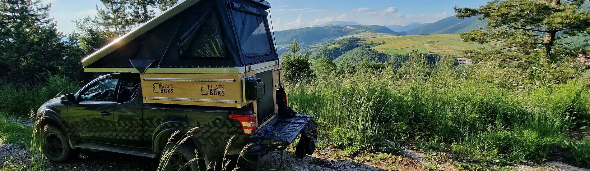Pick-up mit Kabine und aufgeklapptem Dach auf einer Schotterpiste mit Aussicht ins Tal