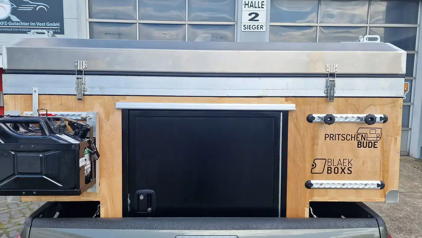 Rückseite einer kompakten Wohnkabine PUR von Pritschenbude mit Alu-Dach und integriertem Stauraumsystem auf einer Pick-up-Ladefläche.