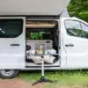 Weißer Yucon 51 FB Campervan mit geöffnetem Schiebetür, ausfahrbarer Markise und Blick auf Küche und Wohnbereich, dazu ein gedeckter Campingtisch davor.