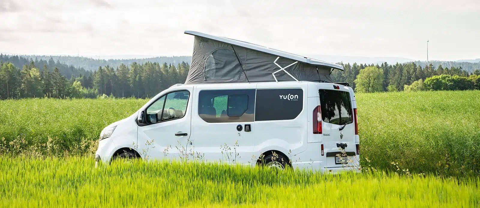 Yucon 55 SB FEVER Campervan mit geöffnetem Aufstelldach auf einer Wiese, Seitenansicht, Natur im Hintergrund.