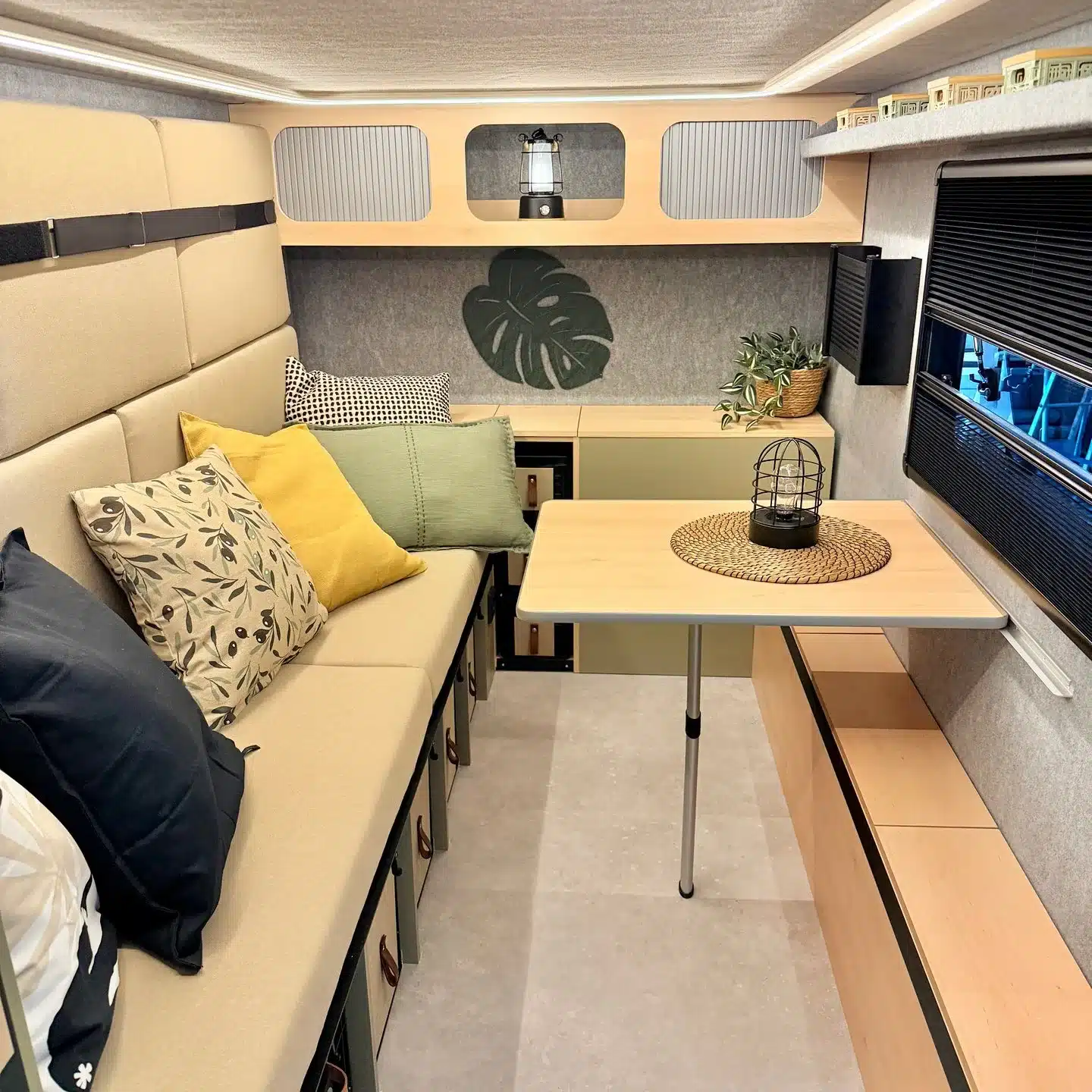 Innenraum des 7even50 Biker & Family Wohnwagens mit Sitzbank, Tisch, Kissen und Stauboxen.