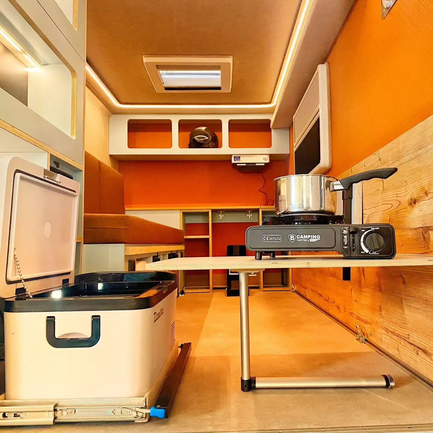 Innenansicht des 7even50 Biker & Family Wohnwagens mit offenem Kühlfach, Gaskocher und Stauraum