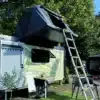 Wohnwagen 7even50 Biker & Family mit aufgebautem Dachzelt, Leiter und Campingtisch im Freien.