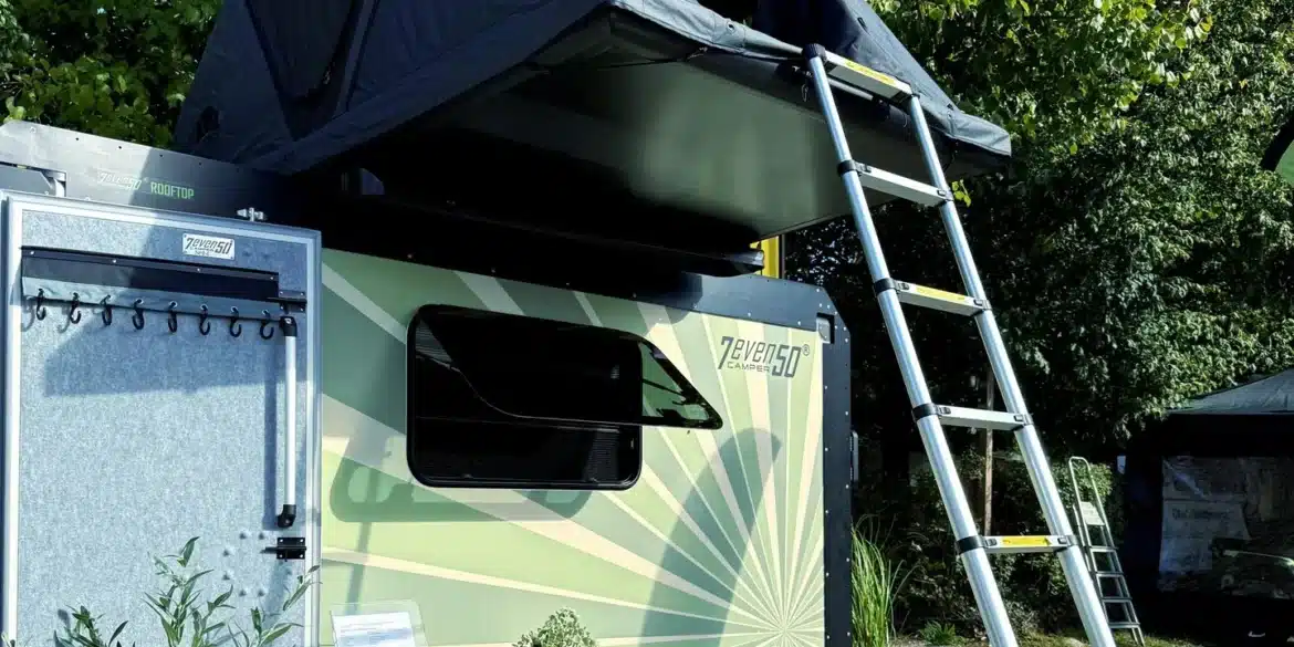 Wohnwagen 7even50 Biker & Family mit aufgebautem Dachzelt, Leiter und Campingtisch im Freien.