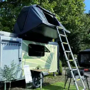 Wohnwagen 7even50 Biker & Family mit aufgebautem Dachzelt, Leiter und Campingtisch im Freien.