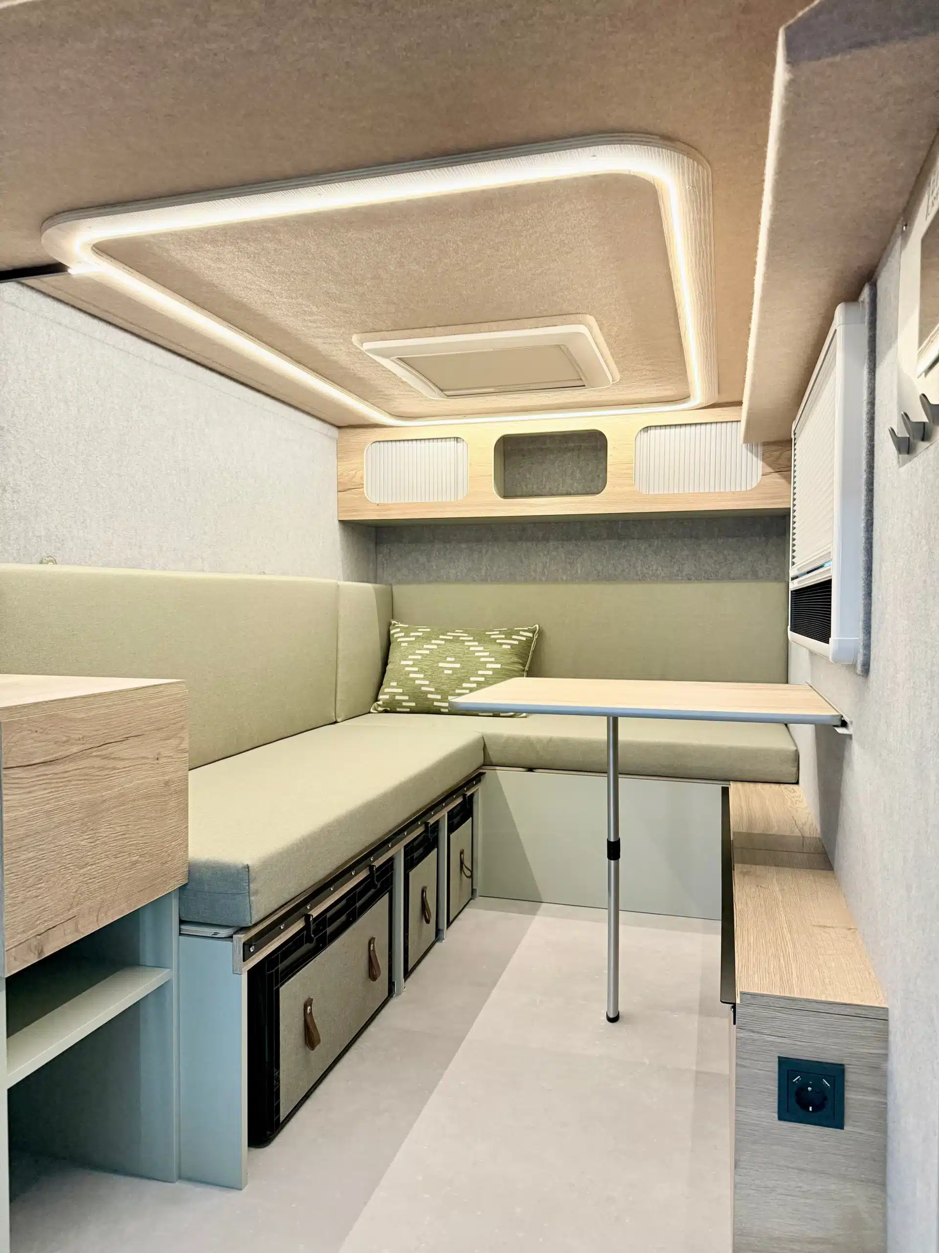 Heller Innenraum eines kompakten Mini-Wohnwagens mit Sitzbank, Tisch, Stauraum und LED-Beleuchtung.