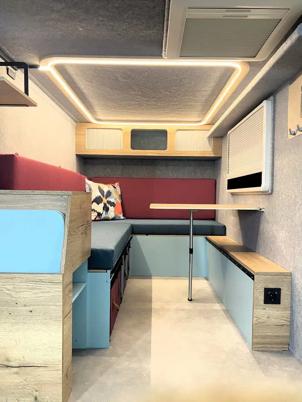 Moderner Innenraum eines Mini-Wohnwagens mit Sitzbereich, abnehmbarem Tisch, LED-Deckenbeleuchtung und Stauraumlösungen