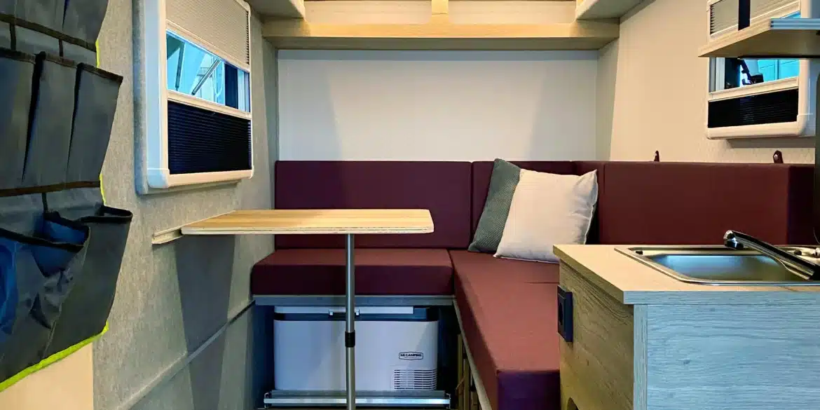 Blick in den modern ausgestatteten Innenraum des 7even50 One Mini-Wohnwagens mit Sitzecke, Klapptisch, Küchenzeile und Dachluke