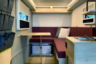 Blick in den modern ausgestatteten Innenraum des 7even50 One Mini-Wohnwagens mit Sitzecke, Klapptisch, Küchenzeile und Dachluke
