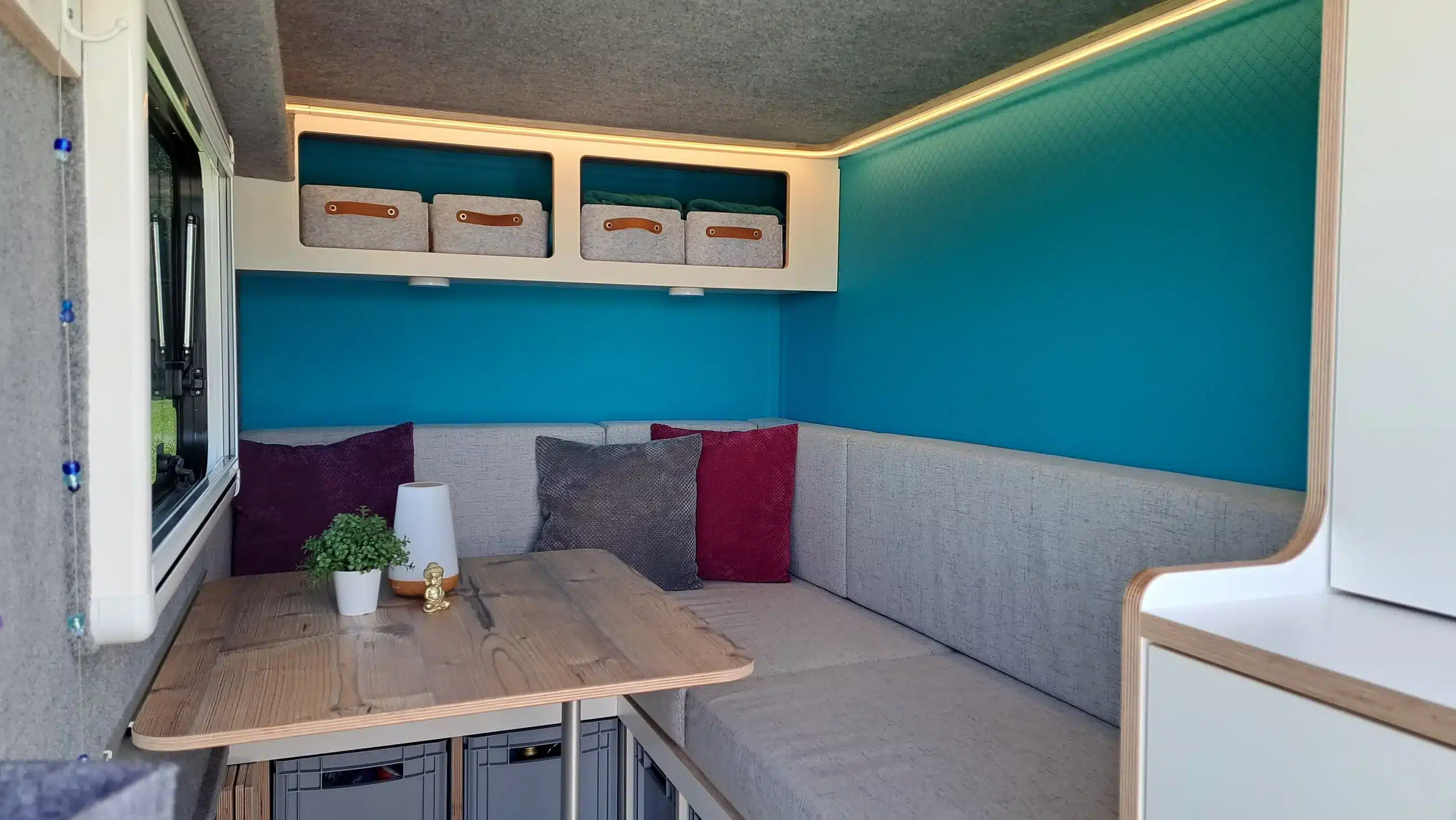 Heller, moderner Innenraum eines 7even50 One Mini-Wohnwagens mit gepolsterter Sitzecke, Holztisch und praktischen Staufächern.