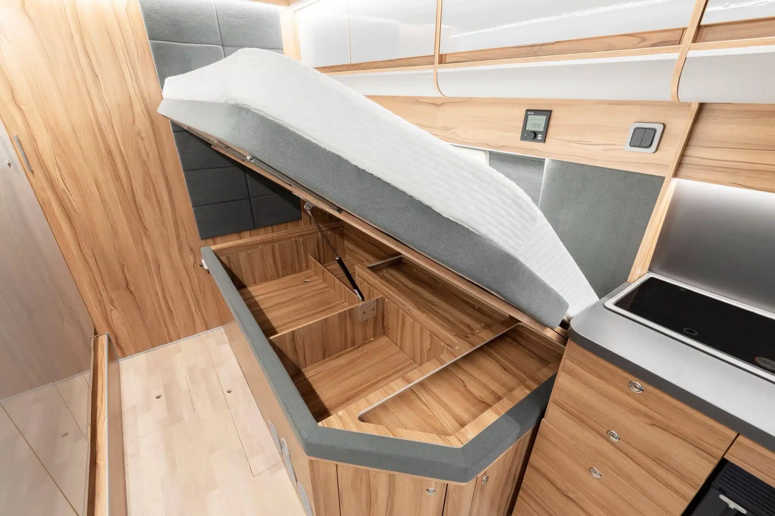 Geöffneter Bettkasten mit großem Stauraum im Affinity Duo Campervan, Holzverkleidung und seitlicher Blick auf die Küche.