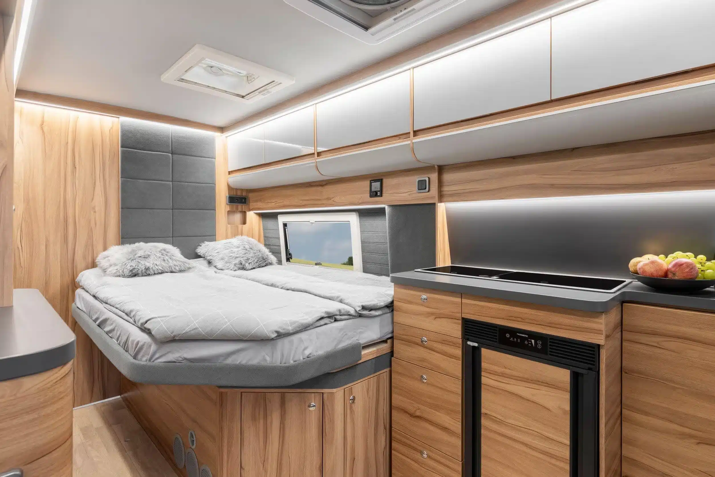 Innenraum des Affinity Duo Campervans mit ausziehbarem französischem Bett, Küchenzeile, Schränken und Holzdekor.