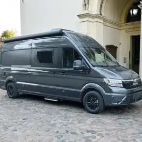 Seitenansicht eines grauen Affinity DUO M Kastenwagens auf MAN TGE Basis vor einem Gebäude, geeignet für komfortables Reisen zu zweit.