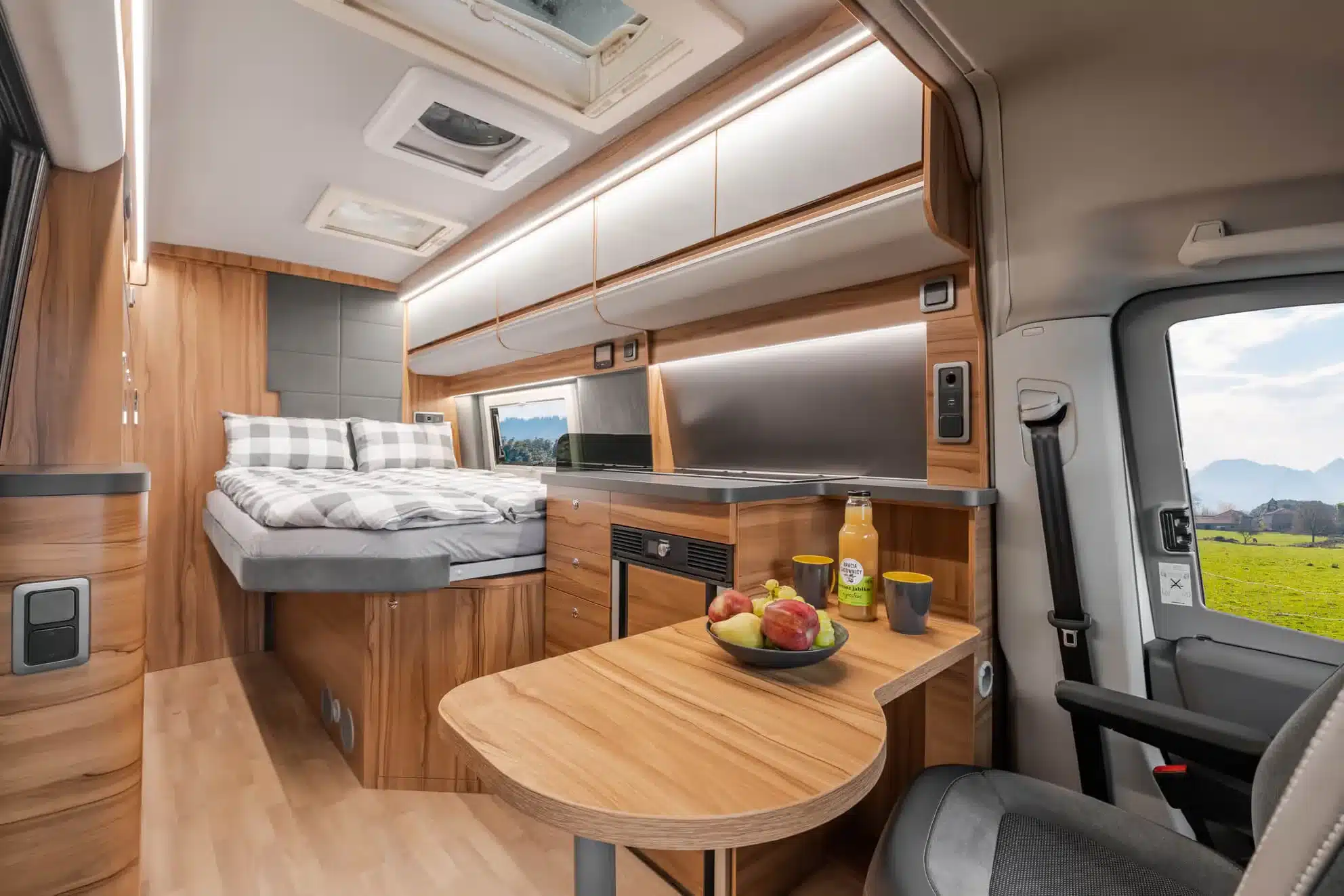 Innenansicht eines Affinity DUO M Campervans mit Bett, Küchenzeile und Esstisch aus Holz.