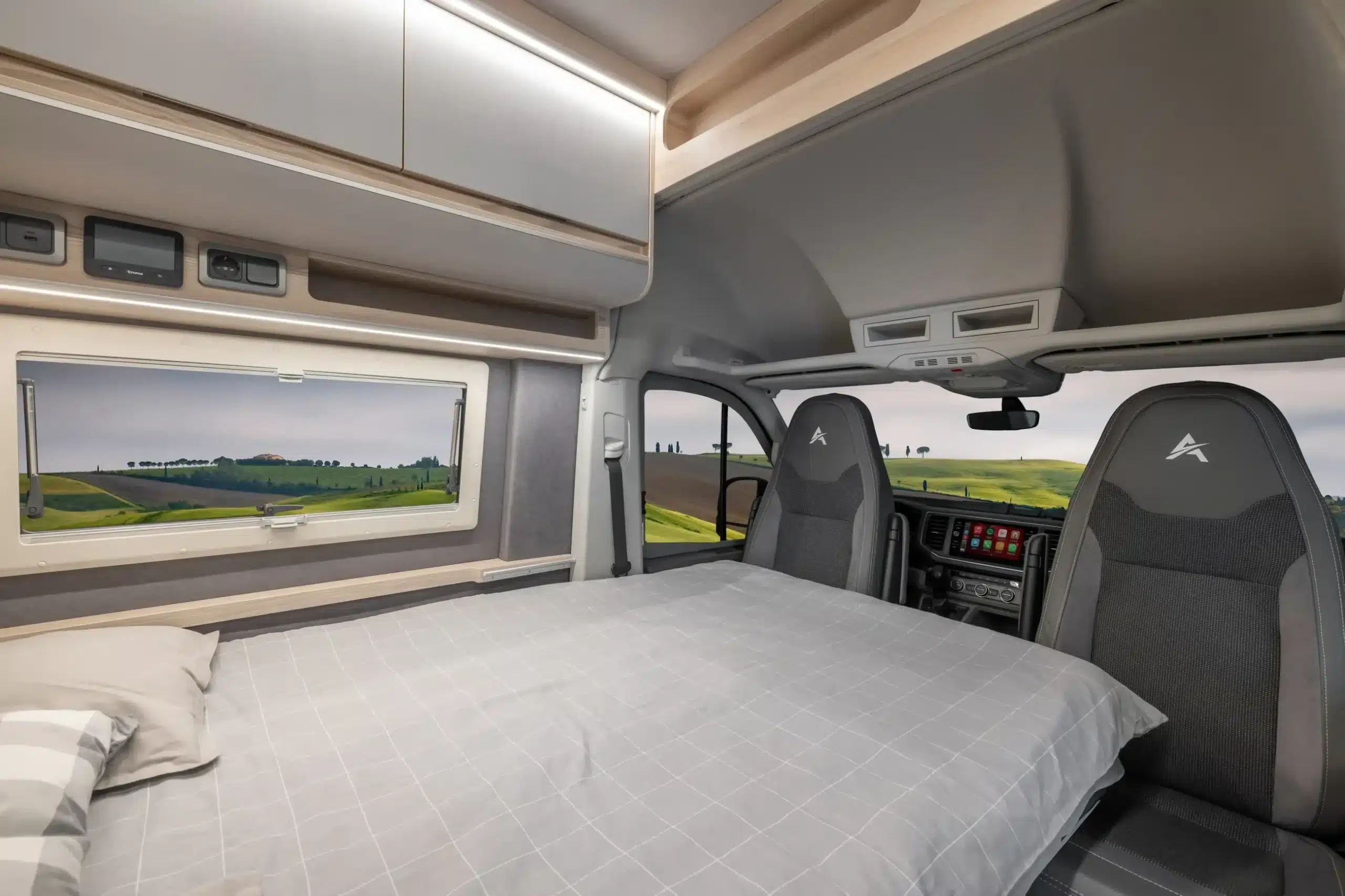 Umgebautes Doppelbett im Wohnraum des Affinity M Four auf MAN TGE Basis, moderne Schränke, Fahrerhaus und Fenster mit Landschaftsausblick.