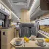Innenraumaufnahme eines Affinity M Three Kastenwagens mit Sitzgruppe, Esstisch, moderner Küchenzeile und Bett im Heck.