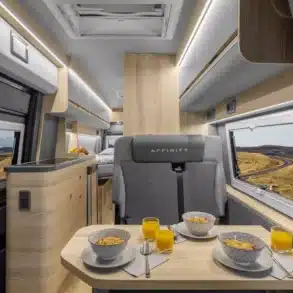 Innenraumaufnahme eines Affinity M Three Kastenwagens mit Sitzgruppe, Esstisch, moderner Küchenzeile und Bett im Heck.
