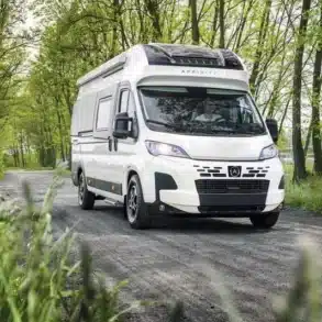 AFFINITY ONE Kastenwagen fährt auf einer Waldstraße, umgeben von Bäumen und grünem Gras.