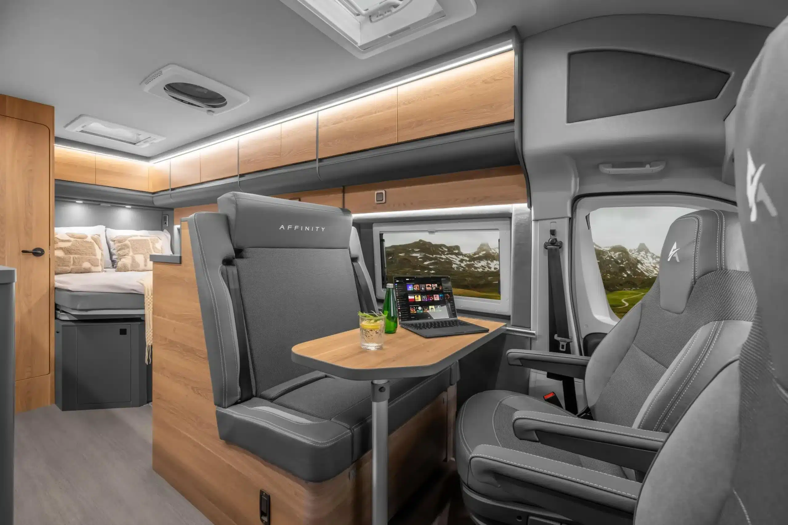 Moderner Innenraum des AFFINITY ONE Campervans mit L-förmiger Sitzgruppe, Tisch, bequemen Sitzen und Bett im Heck.