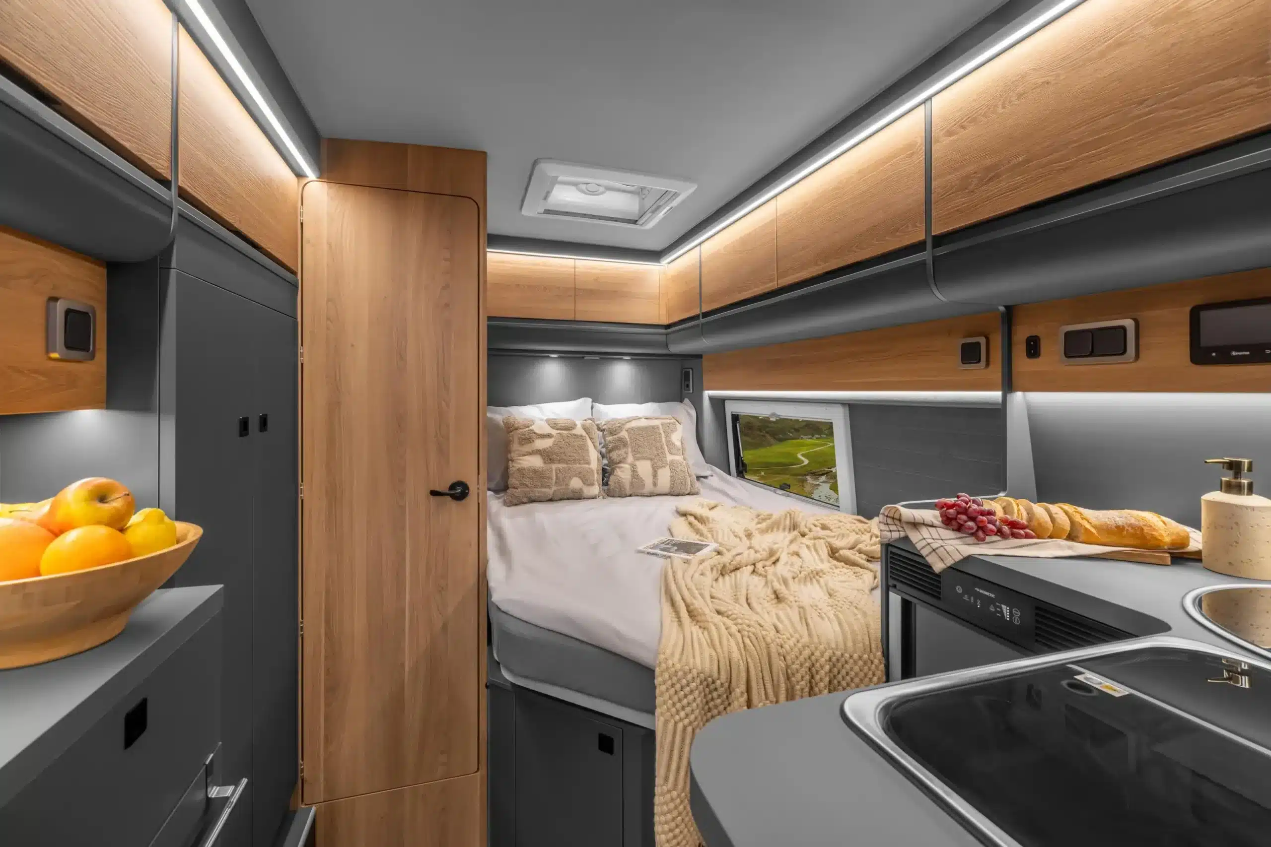Der Innenraum des AFFINITY ONE Campervans mit einem französischen Bett, moderner L-Küche, Holzfronten und großem Stauraum.
