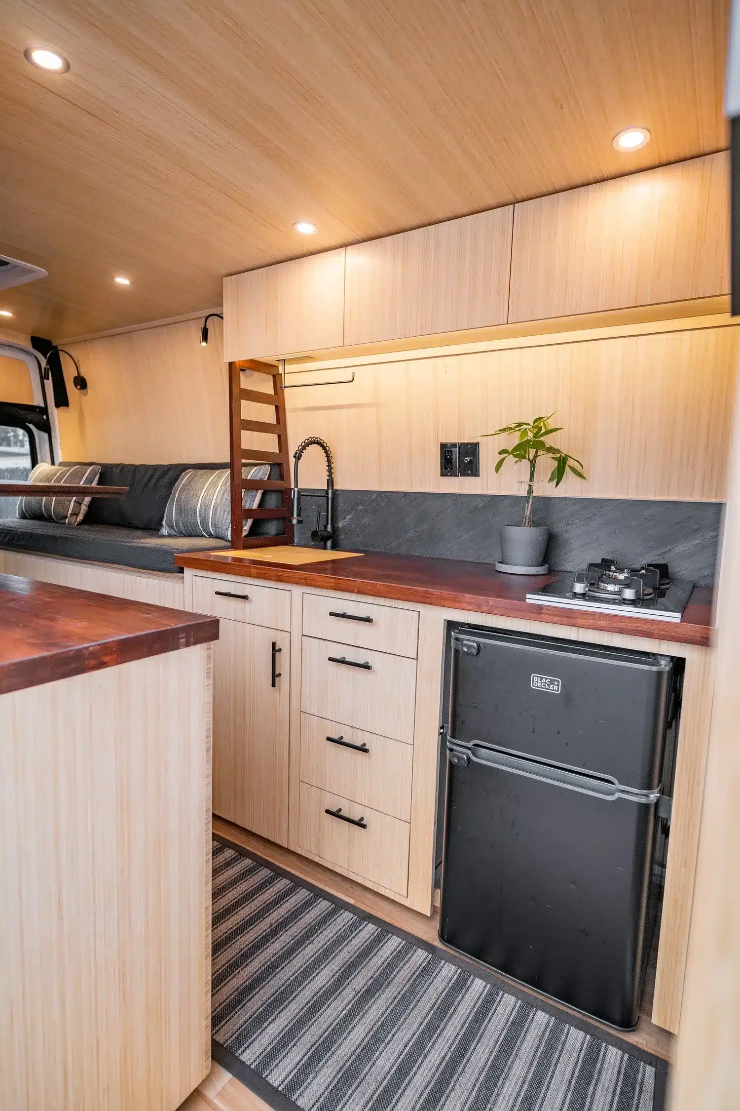 Küche und Wohnbereich im Campervan Appa mit Bambus, Holzoberflächen und Kompaktkühlschrank.