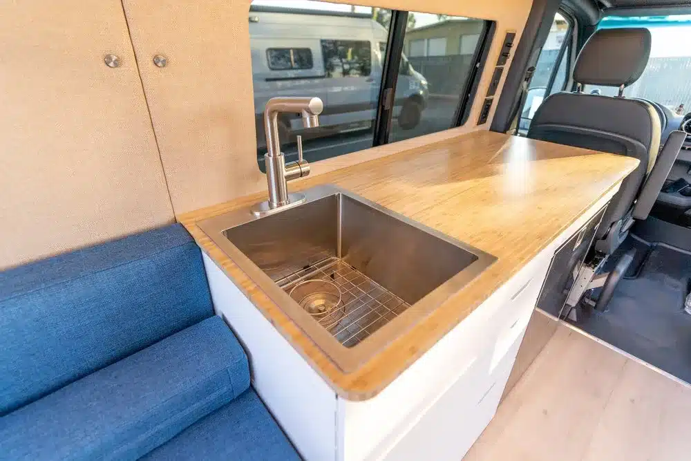 Innenraum eines Base Camp 2 Campervans mit großem rechteckigem Spülbecken, Bambusarbeitsfläche und Sitzbank.