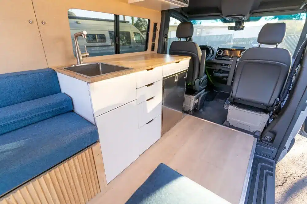 Küchenmodul und Sitzbereich im modernen Base Camp 2 Campervan mit Spülbecken, Stauraum und Fahrerhaus