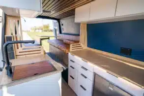 Blick in den modernen, modularen Innenraum eines Base Camp Campervans mit Küchenzeile, Sitzbank und viel Stauraum