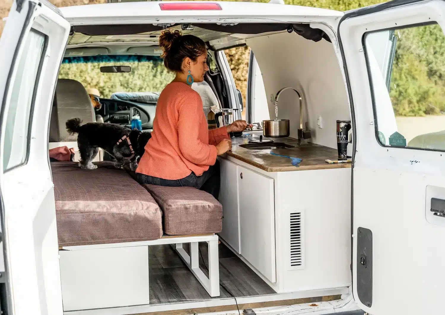 Frau sitzt im Blanca Campervan auf einer ausziehbaren Bank vor der Küche mit Birkenmultiplex-Arbeitsplatte und blauem Epoxy-Fluss.