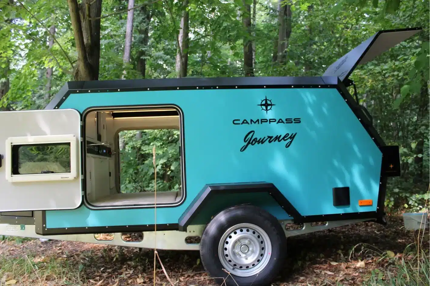 Seitenansicht eines türkisfarbenen Camppass CR400 Journey Micro-Wohnwagens mit geöffneter Tür im Wald.