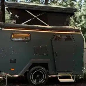 Seitenansicht des Camppass CR455 Offroad-Caravans mit ausgefahrenem Aufstelldach im Wald.