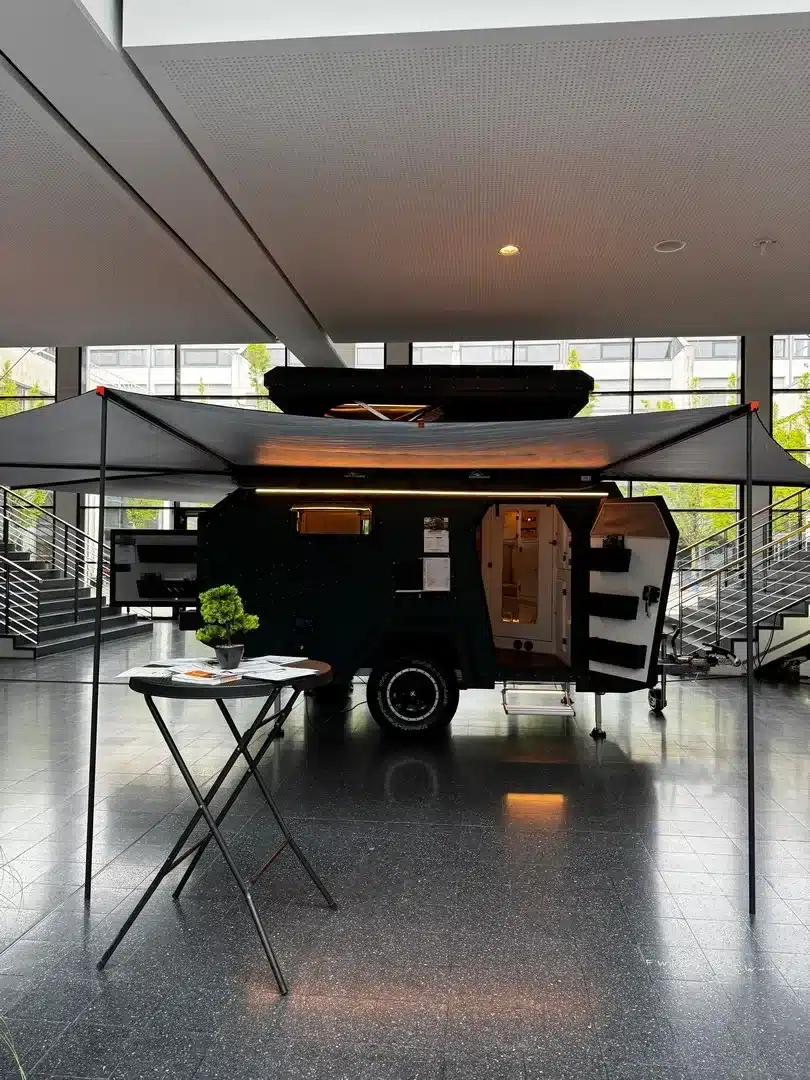 Der Camppass CR455 Offroad-Caravan mit geöffneter Tür und ausgefahrener Markise, ausgestellt in einer modernen Halle.