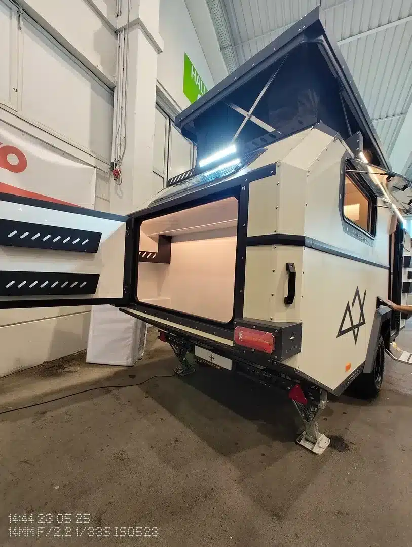 Seitliche Heckansicht des Camppass CR555 Offroad-Campers mit hochgeklapptem Dach und geöffnetem Heckstauraum.