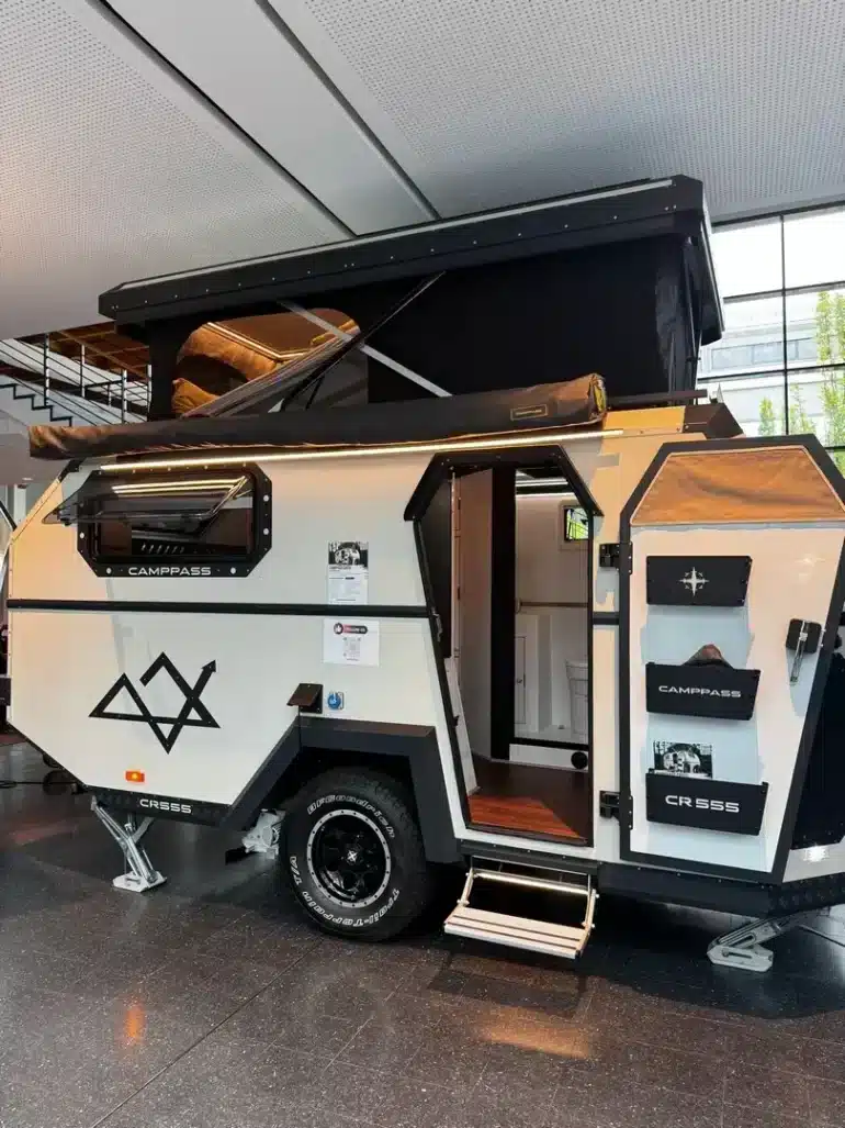 Camppass CR555 Offroad-Camper mit aufgeklapptem Dach und geöffneter Tür, Innenraum teilweise sichtbar.