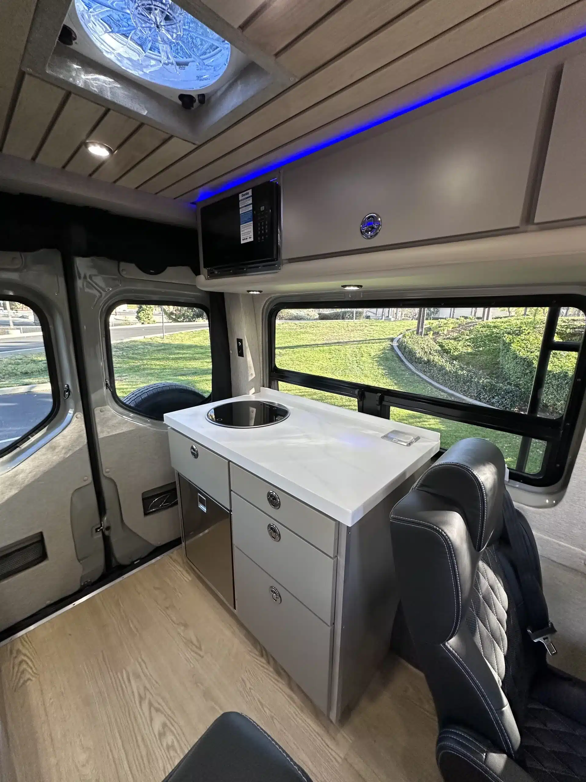 Innenraumansicht des Carpool Cruiser 2024 mit Küchenzeile, Spüle, Kühlschrank, Mikrowelle und Premium-Sitz.