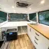 Innenraum eines Chevrolet Astro Campervan mit weißer Bambus-Küchenzeile, Schlafplattform, Bluetti Powerstation und LED-Beleuchtung.