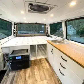 Innenraum eines Chevrolet Astro Campervan mit weißer Bambus-Küchenzeile, Schlafplattform, Bluetti Powerstation und LED-Beleuchtung.