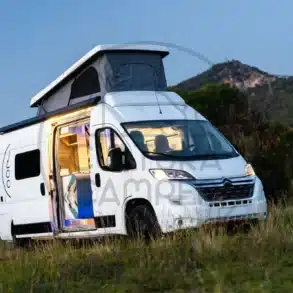 Citroën Jumper L3 H2 Campervan mit geöffnetem Aufstelldach auf einer Lichtung vor Bergen, seitlich aufgenommen